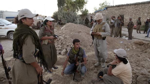 Eine Gruppe bewaffneter Kämpfer steht und sitzt im Freien.