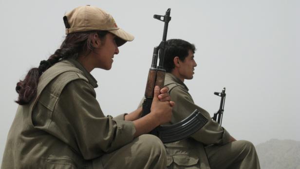 Zwei bewaffnete Personen in Uniform sitzen im Freien.
