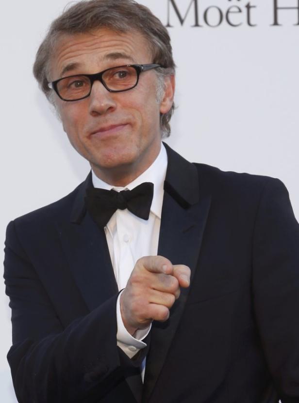 Christoph Waltz in einem schwarzen Smoking mit Fliege zeigt mit dem Finger auf den Betrachter.