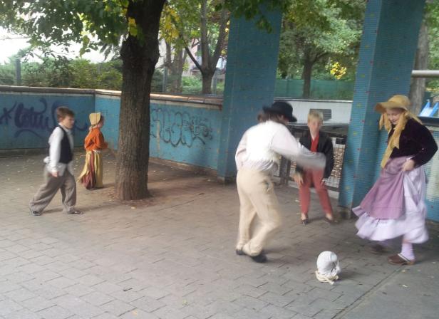 Eine Gruppe von Kindern spielt im Freien in historischen Kostümen.