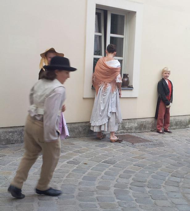 Eine Gruppe von Menschen in historischer Kleidung steht vor einer hellen Wand.