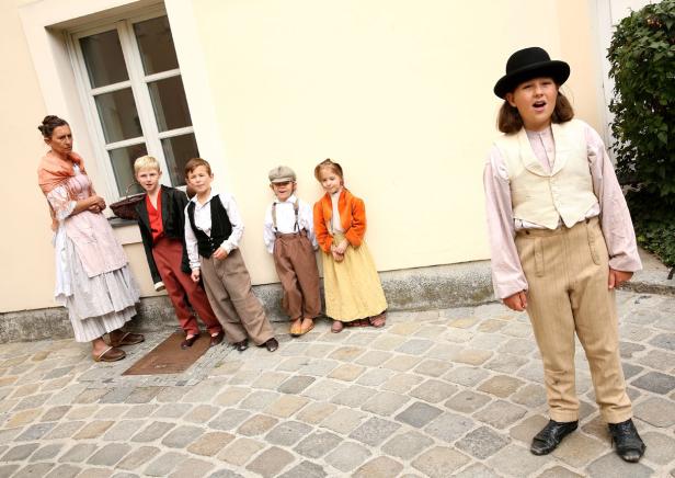 Eine Gruppe von Kindern und eine Frau in historisch anmutenden Kostümen posieren vor einer Wand.