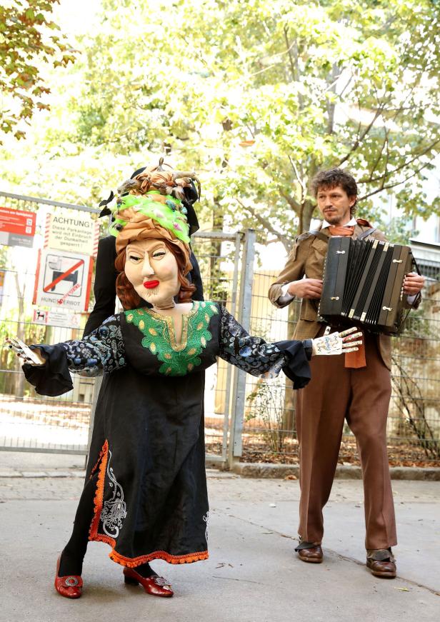 Ein Mann spielt Akkordeon neben einer großen, kostümierten Puppe.