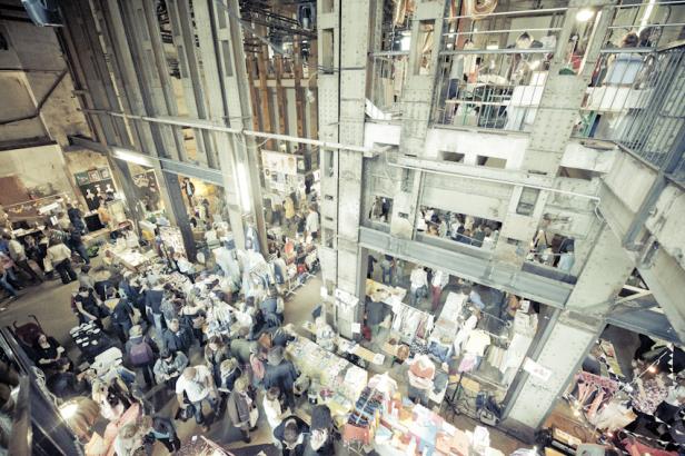 Ein belebter Flohmarkt in einer großen Industriehalle mit mehreren Ebenen.