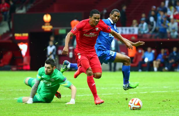 Ein Fußballspieler in Rot läuft auf das Tor zu, während der Torwart in Grün zu fallen versucht.