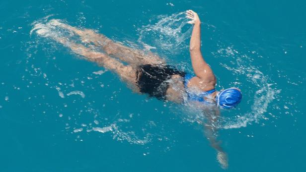 Eine Frau mit blauer Badekappe schwimmt im türkisfarbenen Wasser.