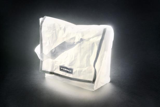 Eine weiße FREITAG-Tasche vor einem dunklen Hintergrund.