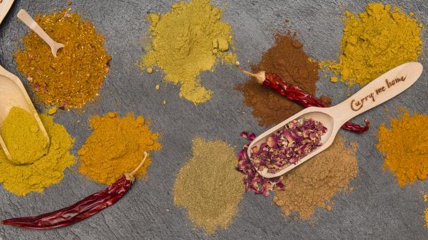 Verschiedene Gewürze und getrocknete Chilischoten sind auf einer dunklen Oberfläche angeordnet.
