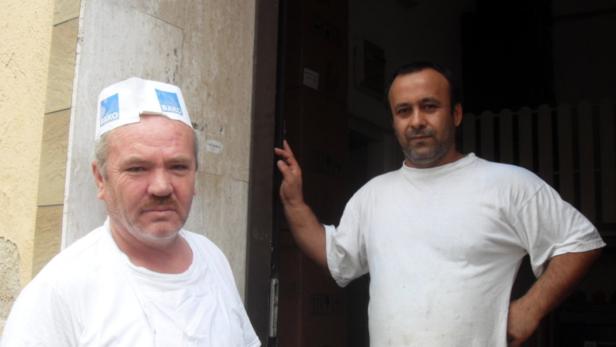 Zwei Männer in weißen T-Shirts stehen vor einem Gebäude.