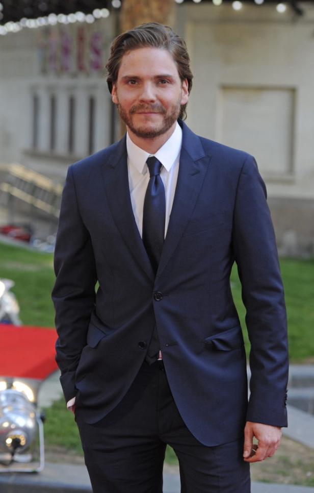 Daniel Brühl in einem dunklen Anzug auf einem roten Teppich.