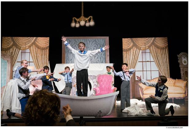 Eine Theaterszene mit Kindern in Kostümen auf einer Bühne vor gemalten Kulissen.