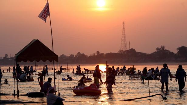 Bei Sonnenuntergang baden Menschen in einem Fluss in Indien.