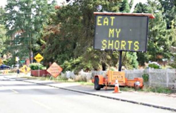 Eine elektronische Anzeigetafel an einer Straßensperre zeigt den Text „Eat my shorts“.