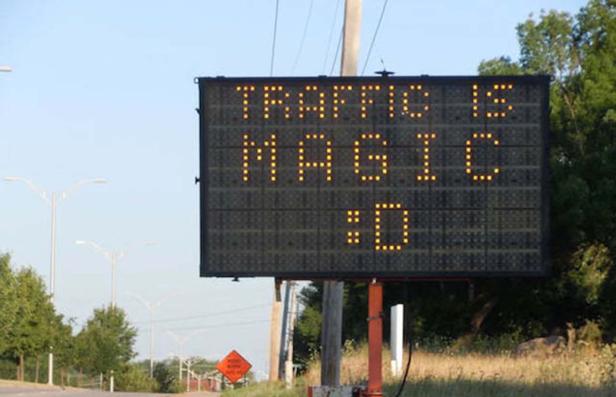 Eine elektronische Anzeigetafel am Straßenrand zeigt die Nachricht „Traffic is magic :D“.
