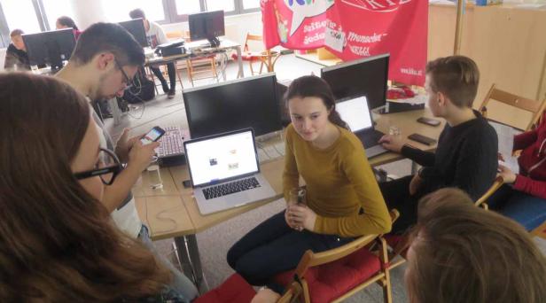 Eine Gruppe von Menschen sitzt an Tischen und arbeitet an Laptops und Computern.
