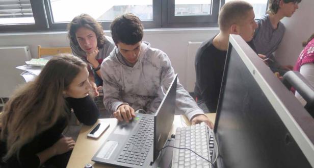 Eine Gruppe von Jugendlichen arbeitet gemeinsam an einem Laptop und einem Computer.