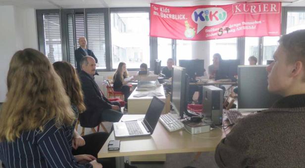 Eine Gruppe von Menschen sitzt in einem Büro unter einem „KiKu Kurier“-Banner.