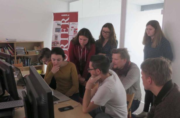 Eine Gruppe von Menschen schaut aufmerksam auf einen Laptop in einem Büro.