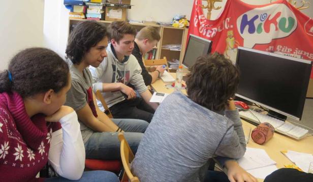 Eine Gruppe Jugendlicher sitzt an einem Tisch und arbeitet an Computern.