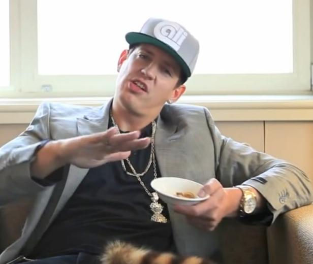 Ein Mann mit Kappe und Schmuck gestikuliert, während er eine Schale hält.