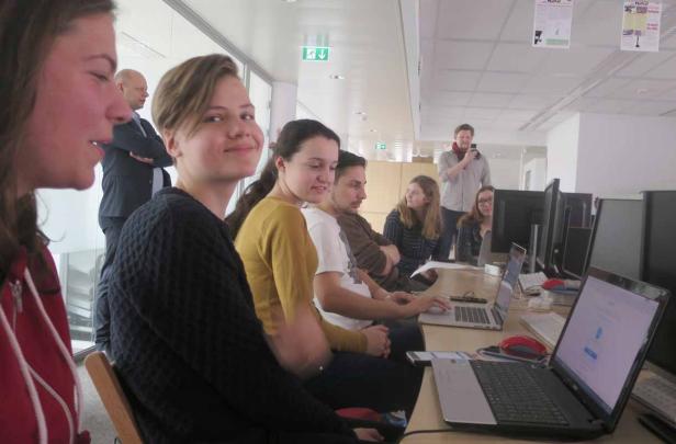 Eine Gruppe junger Leute sitzt an einem Tisch mit Laptops in einem Büro.