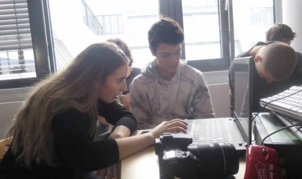 Eine Gruppe junger Leute arbeitet gemeinsam an einem Laptop in einem hellen Raum.
