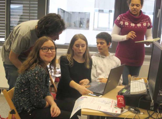 Eine Gruppe junger Leute arbeitet gemeinsam an einem Tisch mit einem Laptop und einem Smartphone.