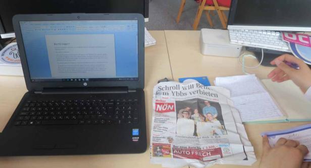 Ein Schreibtisch mit einem Laptop, einer Zeitung und Notizen.