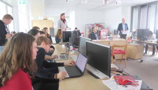 Eine Gruppe von Menschen sitzt an Tischen mit Computern in einem hellen Raum.