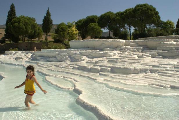 Ein Mädchen watet durch das flache Wasser der Kalksinterterrassen von Pamukkale.