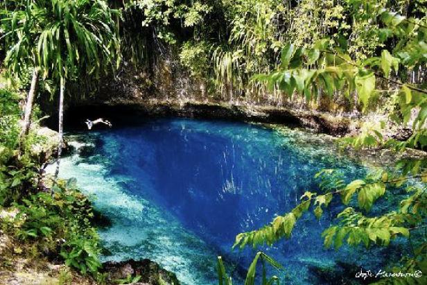 Eine Person springt in ein tiefblaues Wasserloch, umgeben von üppiger Vegetation.