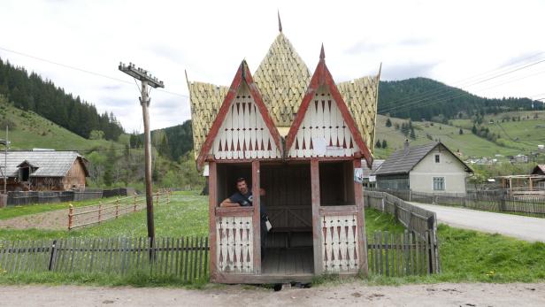 Ein Mann steht in einer verzierten Bushaltestelle in einer ländlichen Gegend.