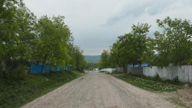 Eine unbefestigte Straße führt durch eine ländliche Gegend mit Zäunen und Bäumen.