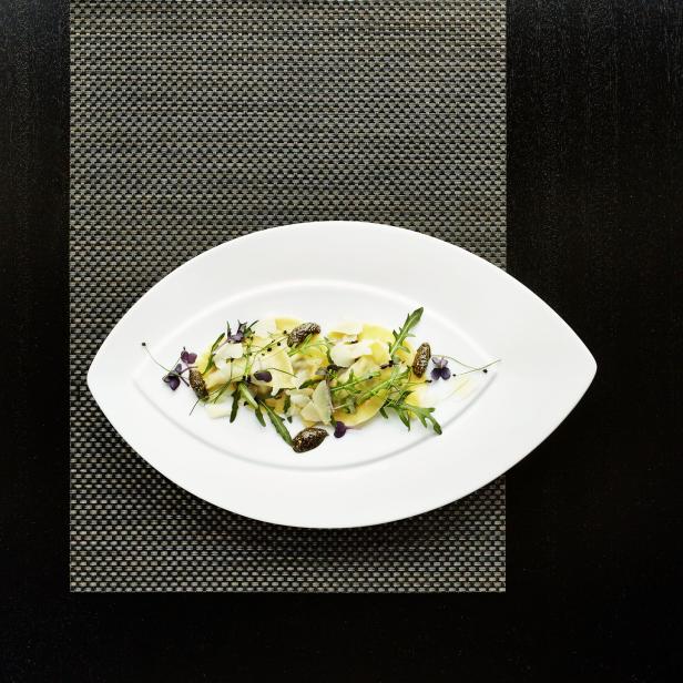 Ravioli mit Rucola, Parmesan und Trüffeln auf einem weißen Teller.