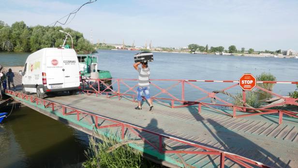 Ein Mann überquert mit einem Koffer auf dem Kopf eine Flussfähre.