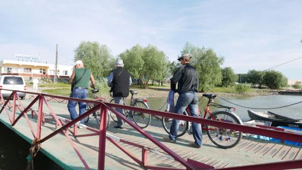 Drei Männer schieben ihre Fahrräder über eine Brücke in Richtung eines Flusses.
