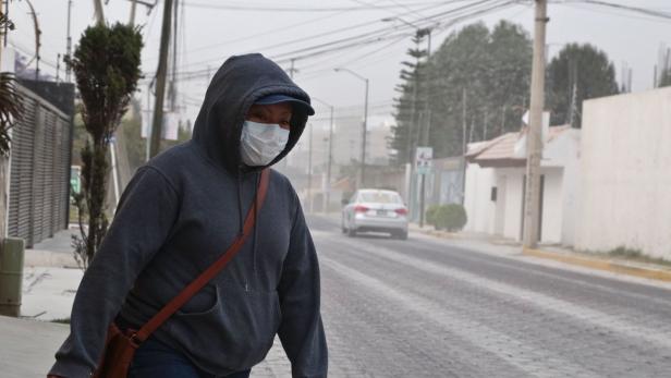 Eine Frau mit Kapuzenpullover und Gesichtsmaske geht eine staubige Straße entlang.