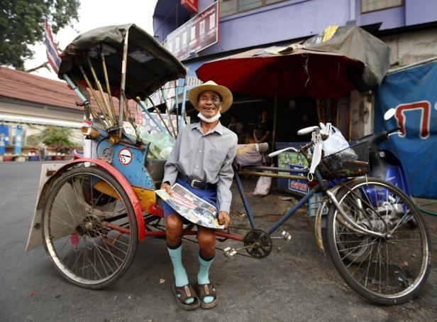 Ein älterer Mann mit Hut sitzt auf einem Fahrradtaxi und liest eine Zeitung.