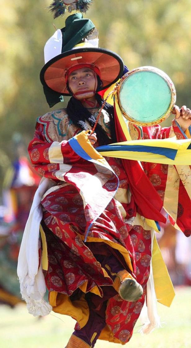 Ein Mann in traditioneller Kleidung tanzt mit einer Trommel.