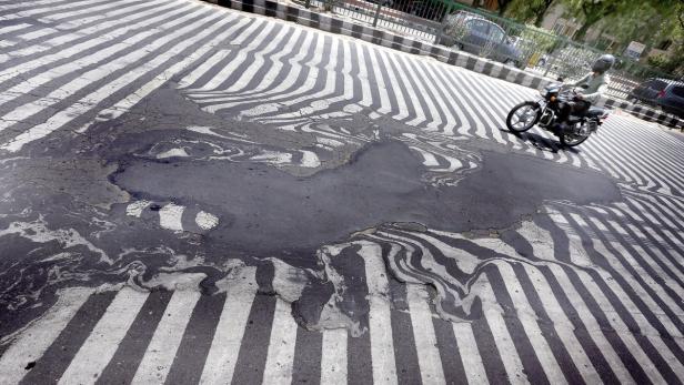 Ein Motorradfahrer fährt über eine beschädigte Straße mit Zebrastreifen.