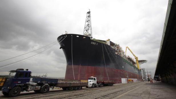 Das Schiff OSX 1 liegt im Hafen vor einem bewölkten Himmel.