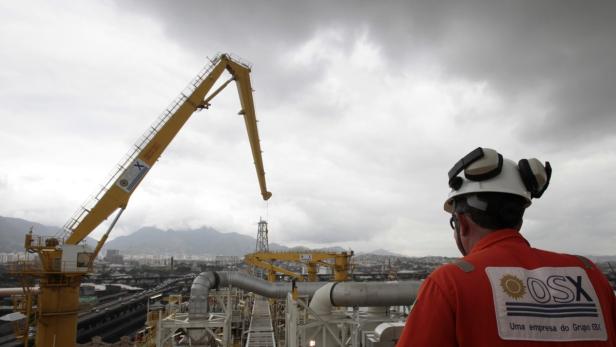 Ein Arbeiter in Arbeitskleidung und Helm blickt auf eine Baustelle mit einem gelben Kran.