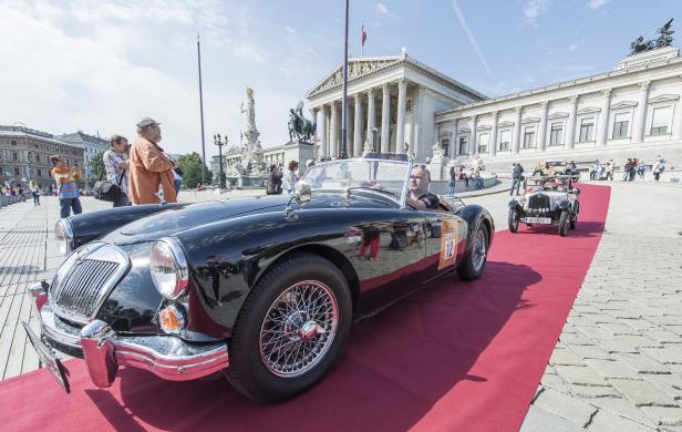 Ein schwarzer Oldtimer fährt auf einem roten Teppich vor dem Wiener Parlament.