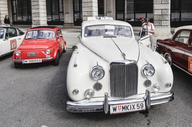 Ein roter Fiat 500 und ein weißer Oldtimer stehen auf der Straße.