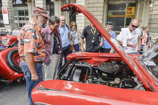 Eine Gruppe von Menschen betrachtet den Motorraum eines roten Oldtimers.