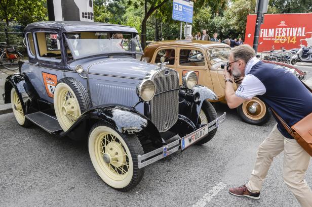 Ein Mann fotografiert zwei Oldtimer vor dem Wiener Rathausplatz Film Festival 2014.
