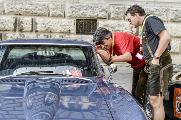Zwei Männer betrachten einen blauen Oldtimer, möglicherweise bei einer Rallye.