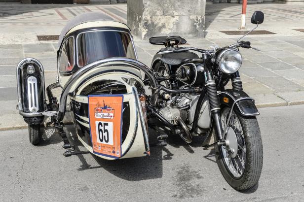 Ein Oldtimer-Motorrad mit Beiwagen, versehen mit der Nummer 65, steht auf der Straße.