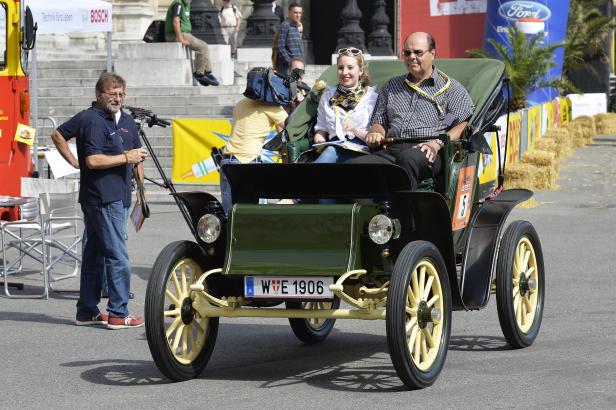 Ein Oldtimer mit der Aufschrift „W E 1906“ fährt auf einer Straße.