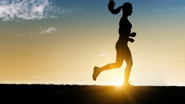 Die Silhouette einer Frau beim Joggen in der Abenddämmerung.